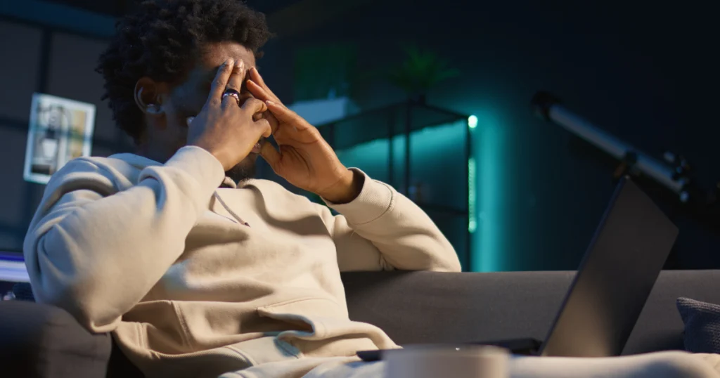 Man feeling mentally overwhelmed while overthinking late at night with a laptop