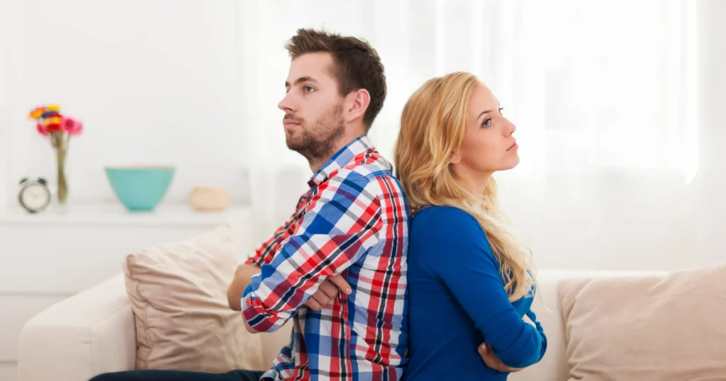 Couple sitting back to back on a couch, showing relationship conflict and emotional distance.