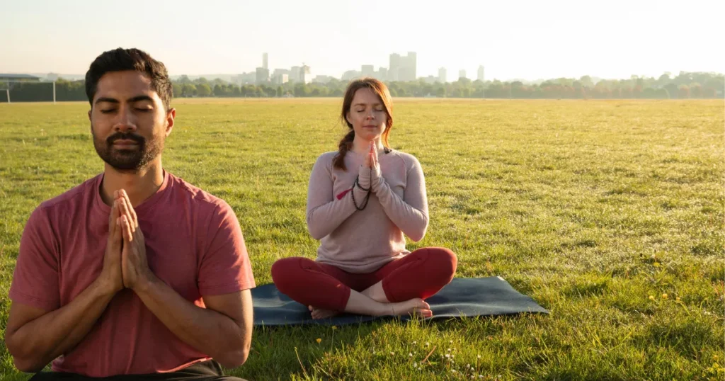 two people meditating on grass with eyes closed in peaceful outdoor setting