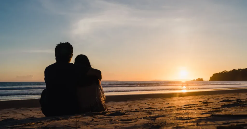 Couple sitting together on a beach during sunset.